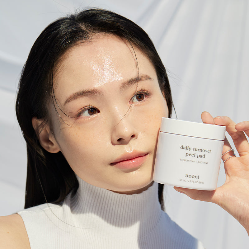 Model holding the Nooni Daily Turnover Peel Pad product showing glowing skin