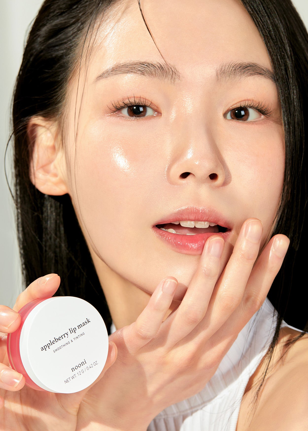 Model with hydrated, glossy lips holding the Nooni appleberry lip mask