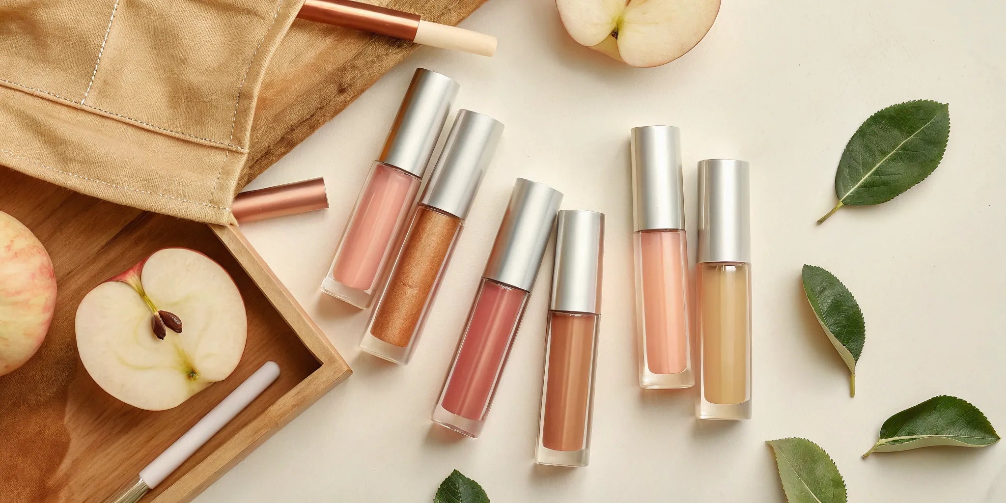 Flat lay of lip oils in soft pink and nude shades with apple slices, K-beauty minimalist style