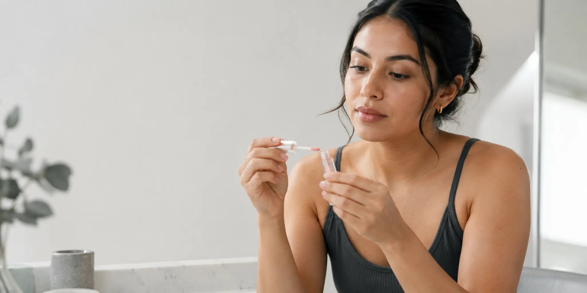 Woman checking a lip oil applicator at a bright vanity