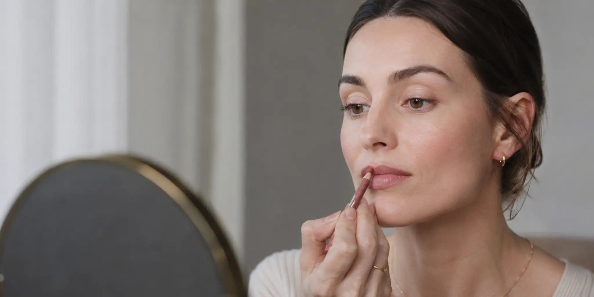 Woman applying neutral rose lip liner before a glossy lip layer