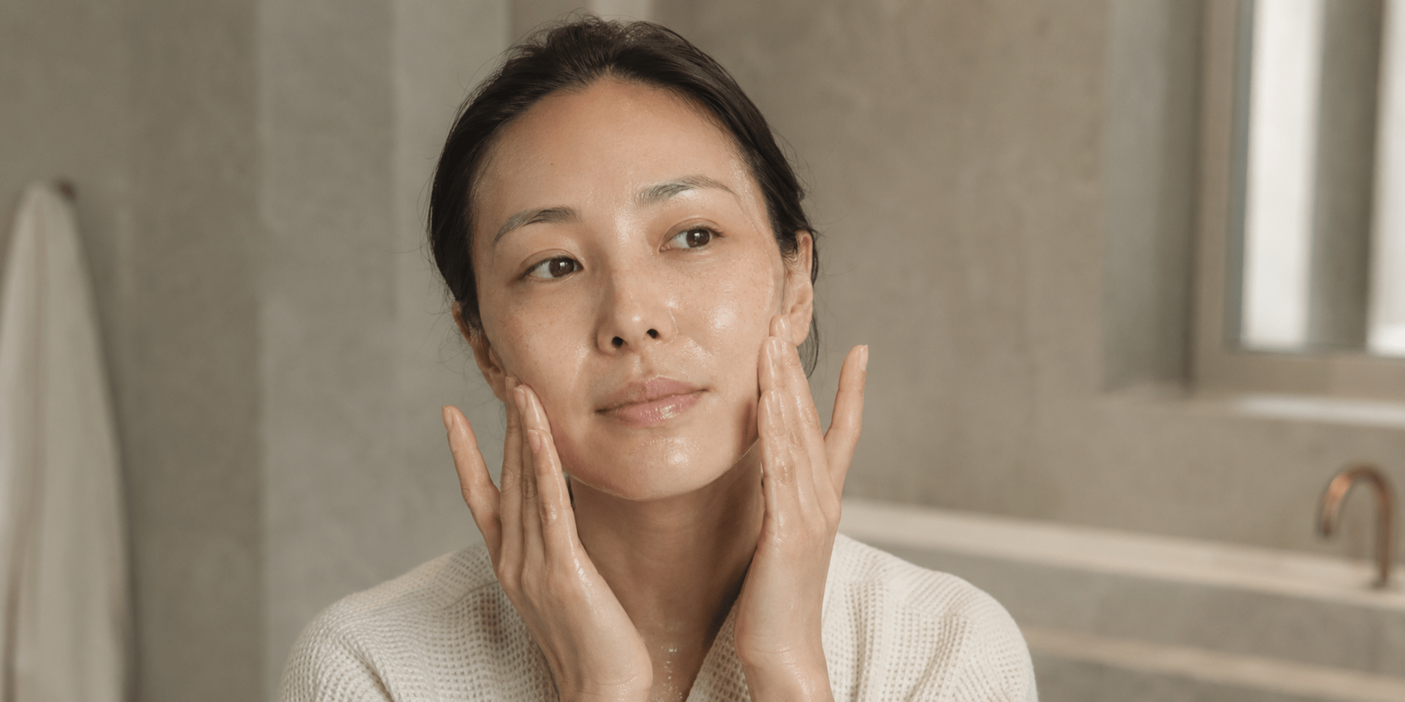 Woman massaging cleansing oil onto bare skin in warm natural light