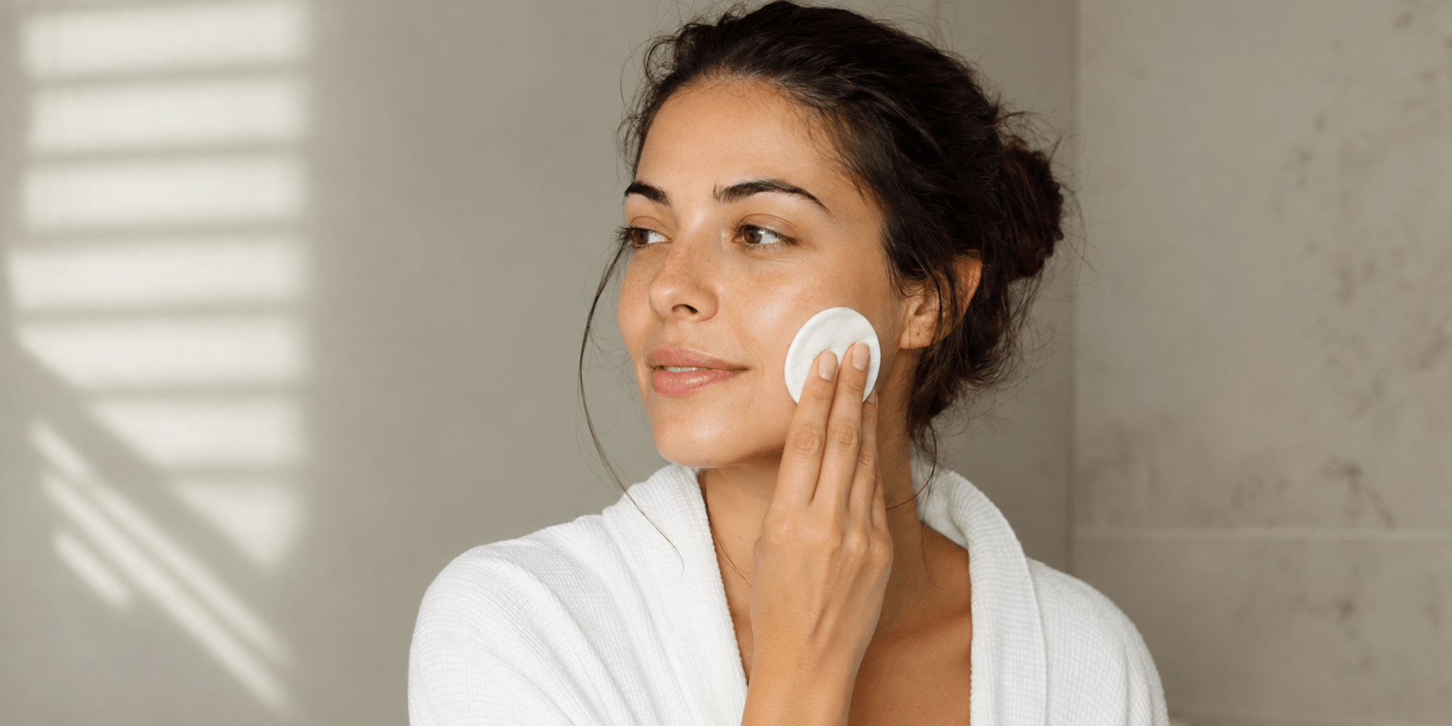 Woman applying a white toner pad to her cheek in warm natural light