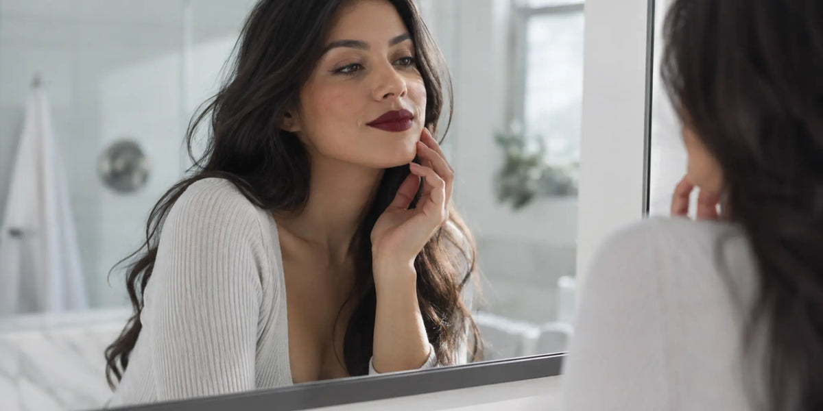 Woman checking a deep burgundy lip look in a bathroom mirror