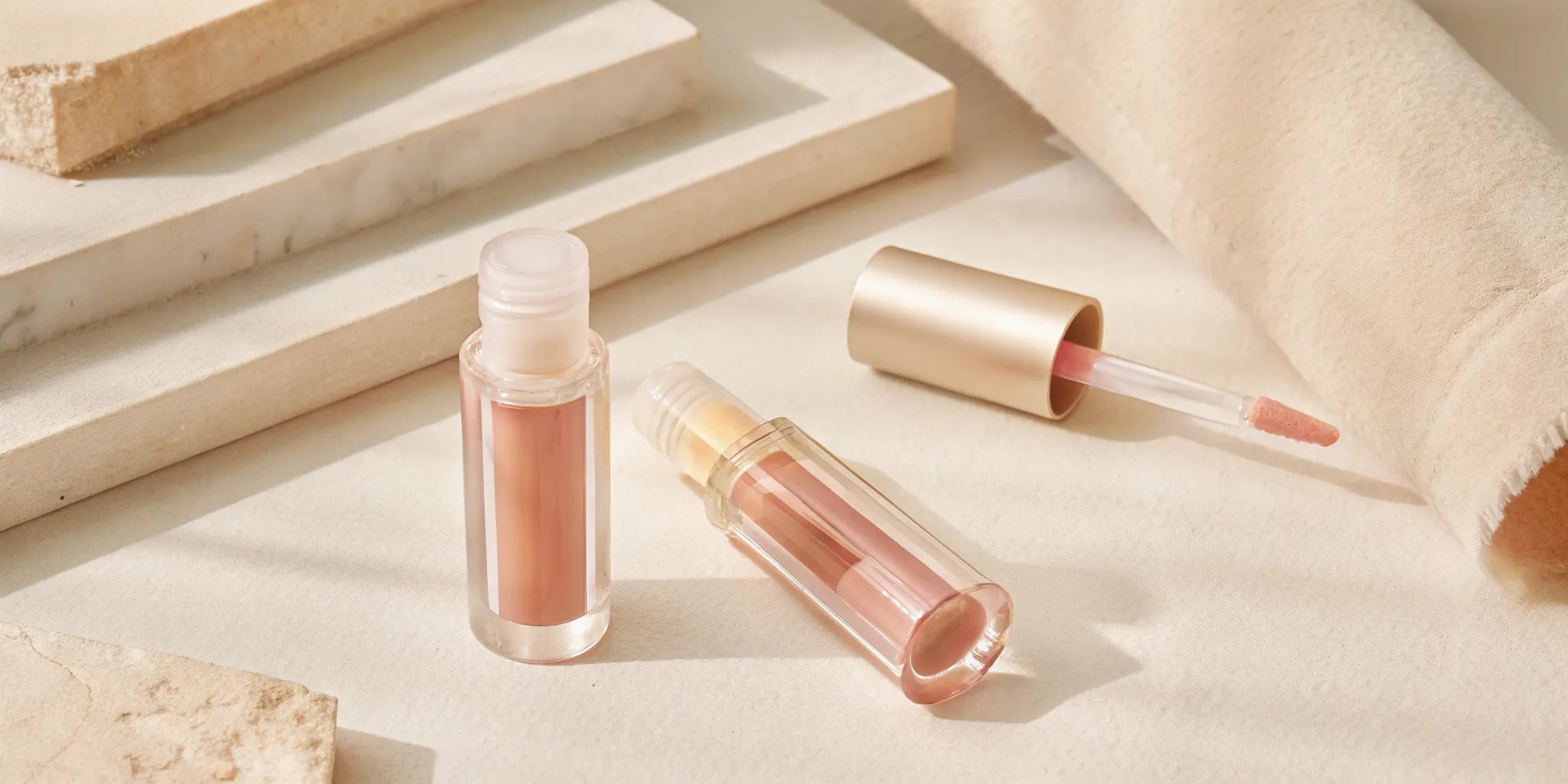 Close-up of a glossy vegan lip oil applicator with pink tinted oil on a clean white background