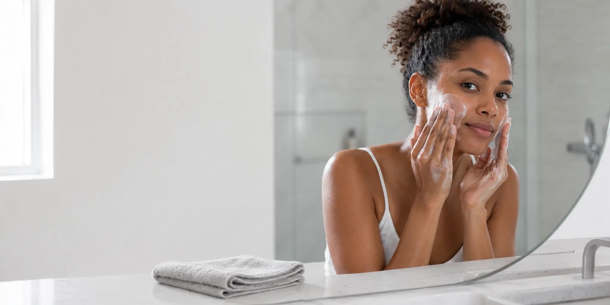 Woman cleansing her face with fingertips beside a folded washcloth